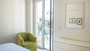 Ein Zimmer mit einem Bett, einem grünen Sessel, einer Schiebeglastür zu einem Außenbereich und einer weißen Kommode mit Schubladen.