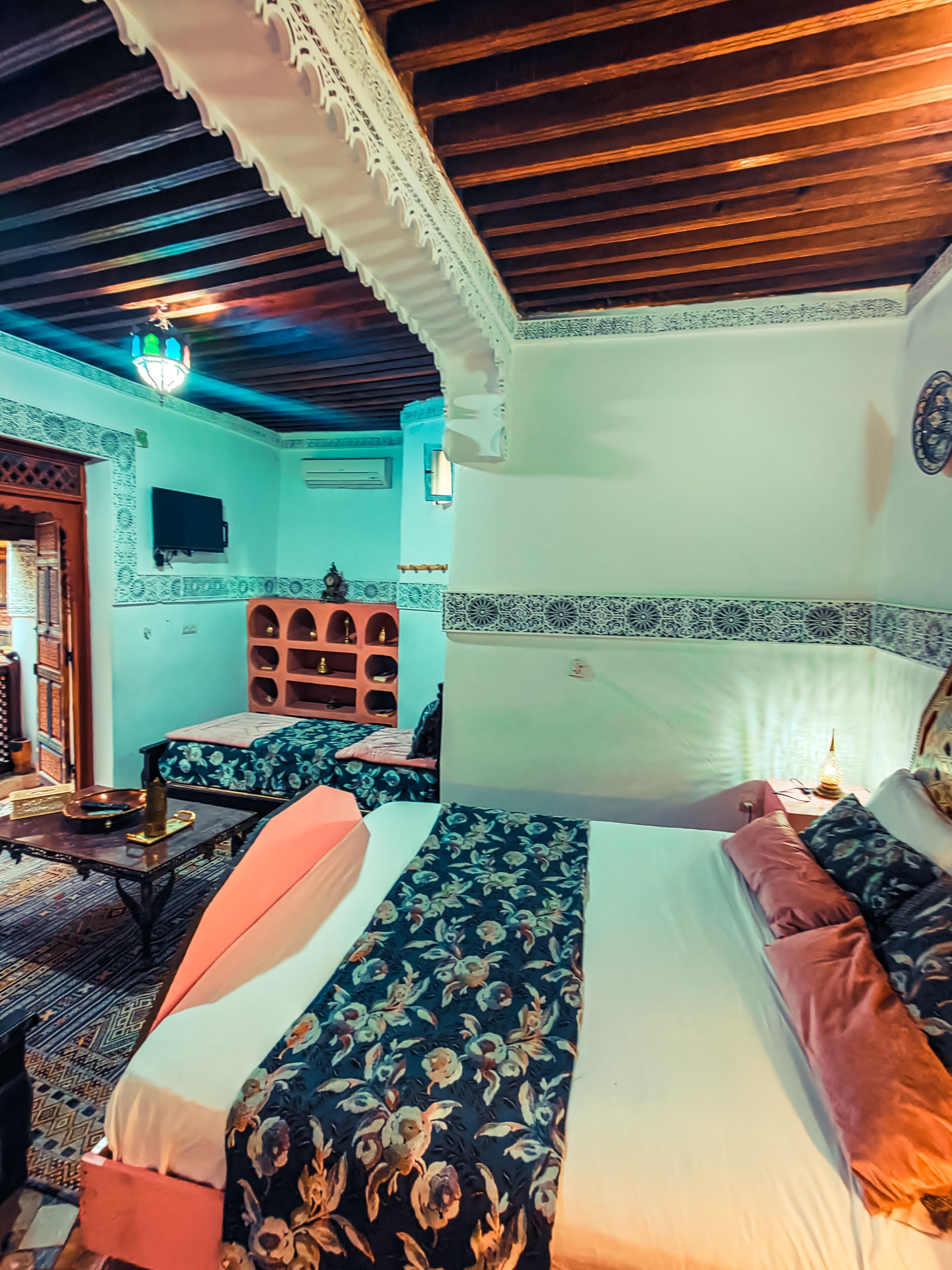 A room with two beds, a wooden ceiling, and patterned walls.