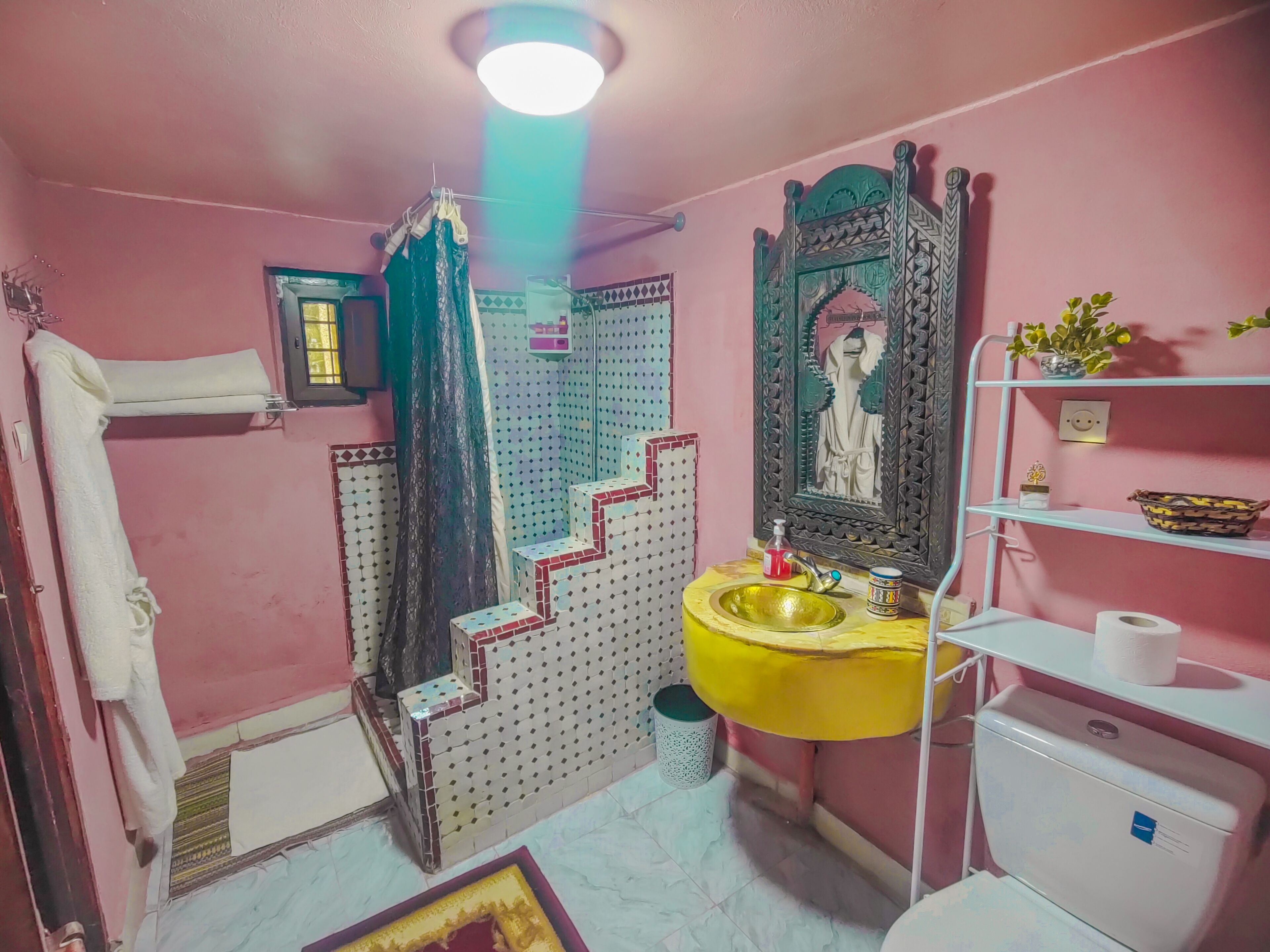 Un baño con lavabo amarillo, espejo con marco decorativo, inodoro y zona de ducha.