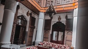 A traditional interior with ornate wooden carvings, a checkered floor, and a central seating area with cushions. - Ryad Zahrat Fes (Fes)