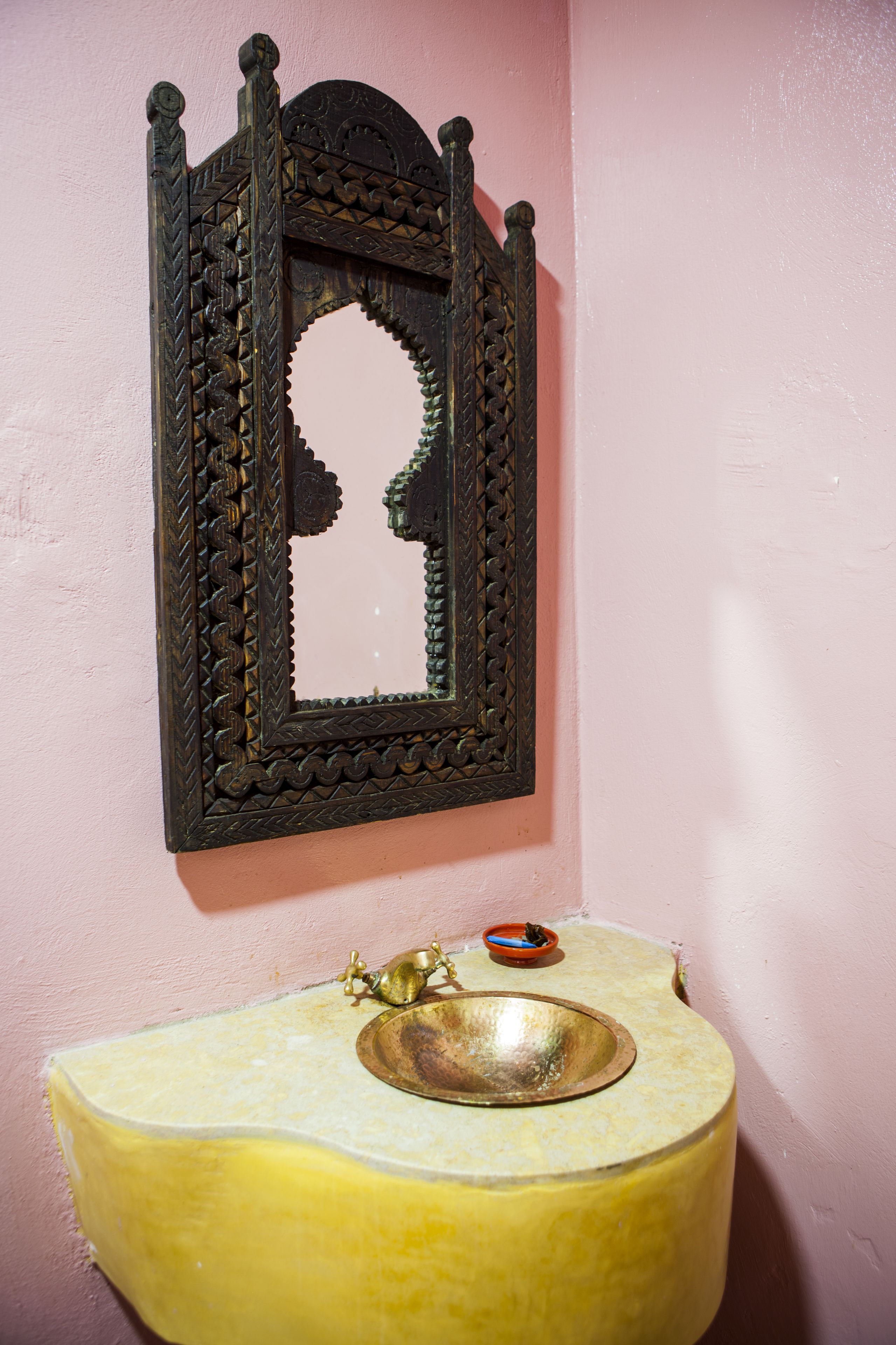 A bathroom with a decorative mirror, a yellow sink, and a small bowl.