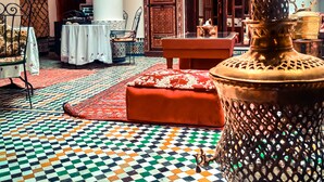 A room with a patterned floor, a large ornate lamp, and a wooden door with intricate designs. - Ryad Zahrat Fes (Fes)