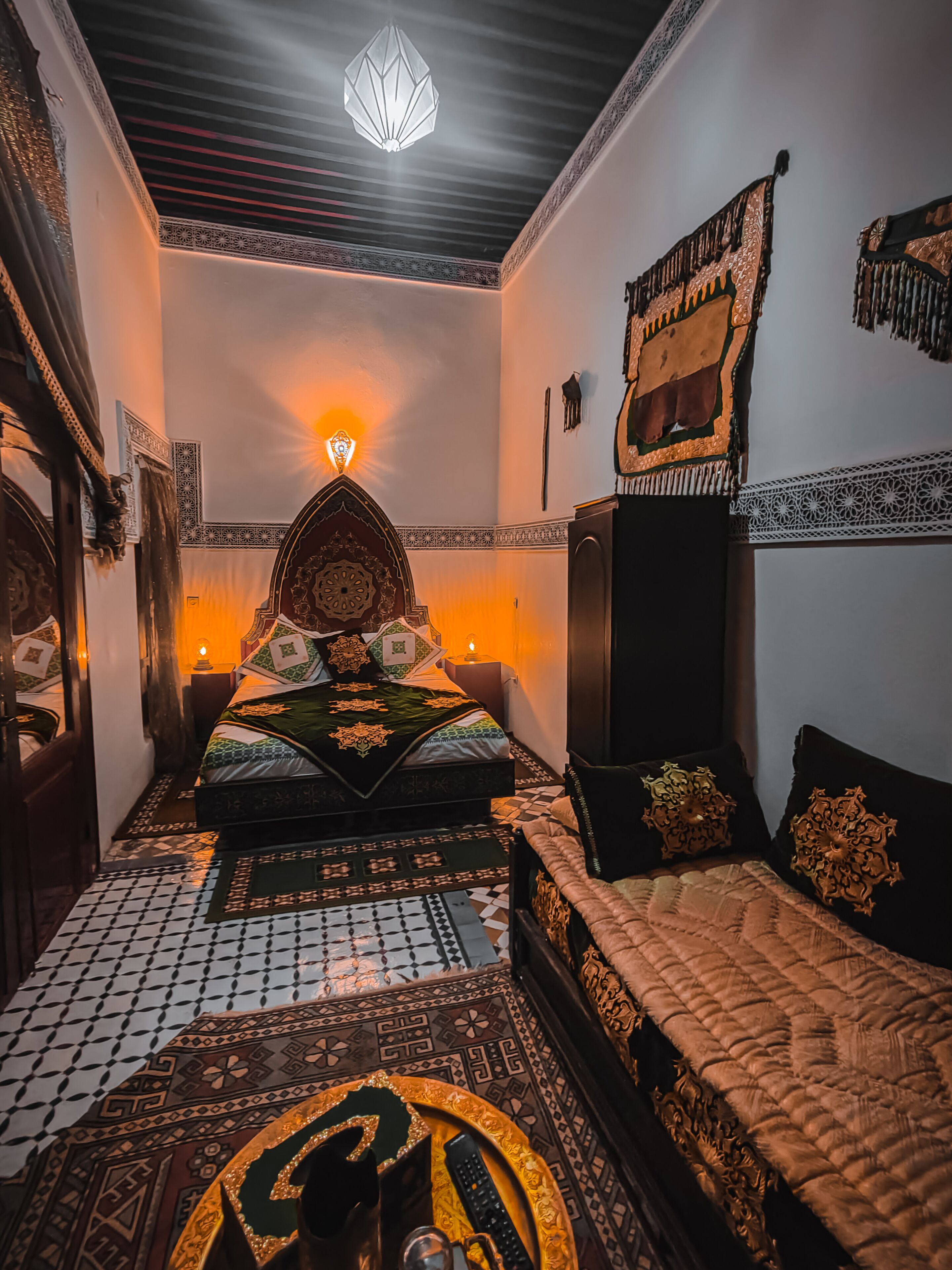 A traditional Moroccan room with a bed, a sofa, patterned rugs, and a decorative wall hanging.