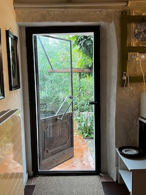 A door leading to a garden with a metal gate, a small shelf with a hat, and a wall-mounted light fixture. - Mansion - Caravate (Caravate)