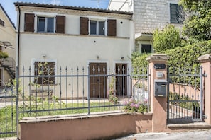 A two-story building with a beige facade, a metal fence, and a gate with a mailbox.
