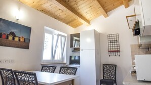 Et spiseområde med et bord og stole, et vindue, et fjernsyn og et køkken med skabe og et køleskab.