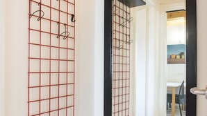 Et værelse med en metalreol med et gittermønster, en dør med sort ramme, og et spejlbillede af et spiseområde med stole og et bord.