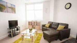 A living room with a sofa, a coffee table, a TV, and a window. - Comfortable Swindon 1 bedroom Town Centre Apartment, FREE Parking (Swindon)