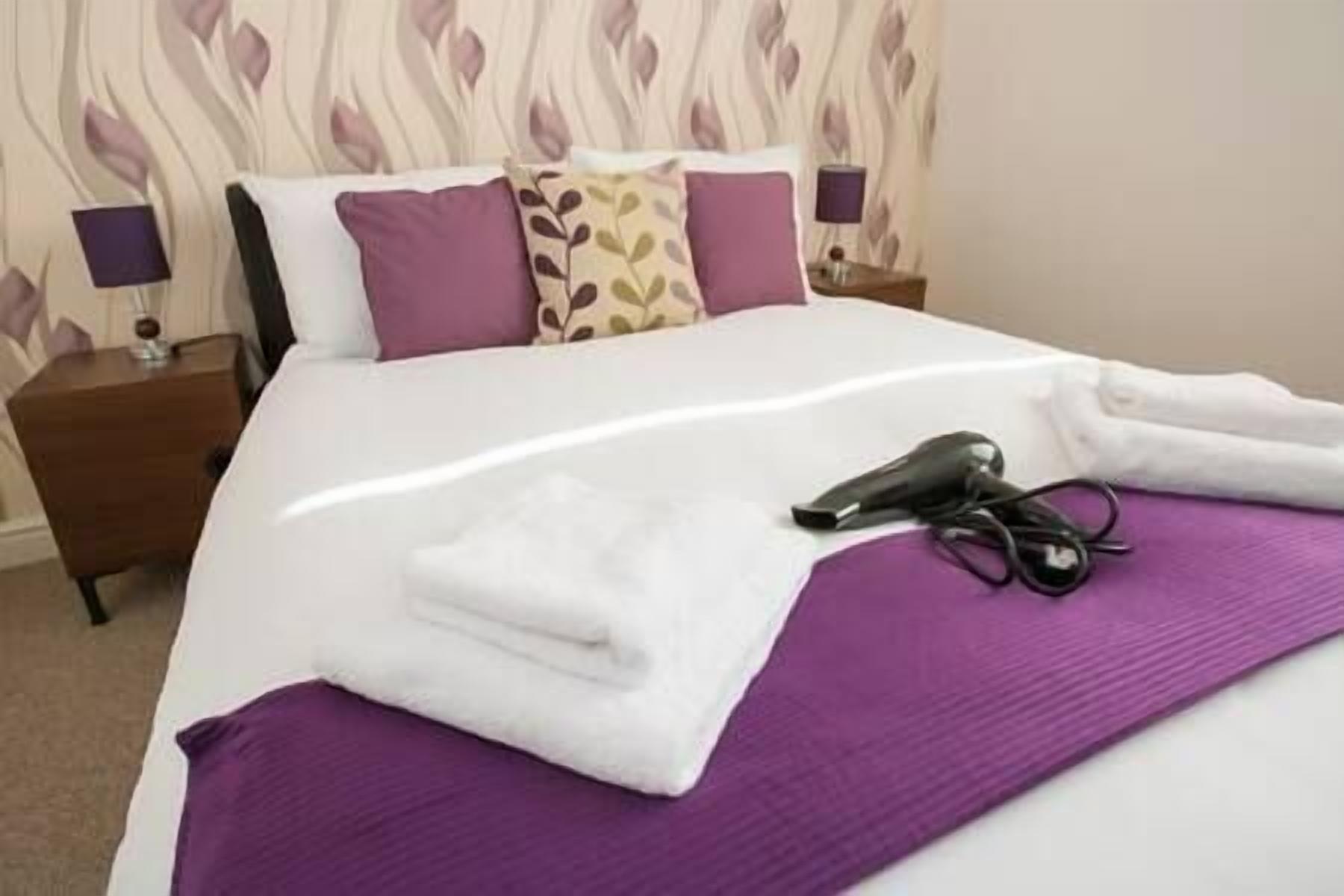A neatly made bed with a purple blanket, a pair of black shoes, and a pair of scissors on the bed.