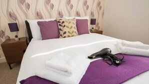 A neatly made bed with a purple blanket, a pair of black shoes, and a pair of scissors on the bed. - Comfortable Swindon 1 bedroom Town Centre Apartment, FREE Parking (Swindon)