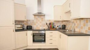 A compact kitchen with white cabinets, a built-in oven, a toaster, and a sink. - Comfortable Swindon 1 bedroom Town Centre Apartment, FREE Parking (Swindon)