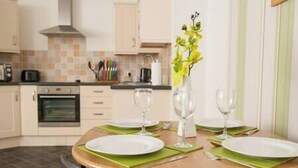 A dining table set for two with plates, cutlery, and glasses, in a kitchen with cabinets and a stove. - Comfortable Swindon 1 bedroom Town Centre Apartment, FREE Parking (Swindon)