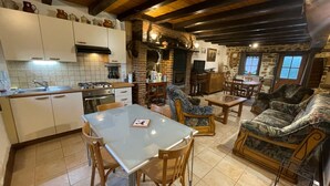 A cozy kitchen with a dining area, featuring a stone fireplace, wooden beams, and a mix of modern and traditional decor. - Charming independent cottage with enclosed garden, pets allowed (La Petite-Marche)
