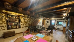 A rustic interior with a stone wall, wooden beams, a staircase, a dining area with a table and chairs, and a kitchen area. - Charming independent cottage with enclosed garden, pets allowed (La Petite-Marche)