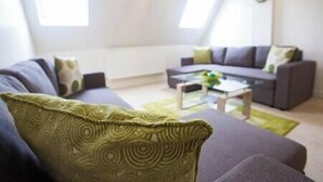 Ein modernes Wohnzimmer mit einer grauen Couch, einem Glastisch und einem grün gemusterten Kissen.