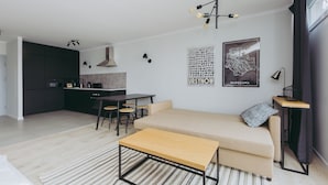 Ett modernt vardagsrum med en soffa, ett soffbord i trä, en matplats med bord och stolar samt ett kök i bakgrunden.