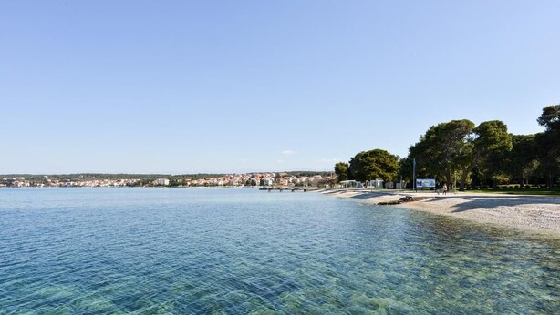 A coastal view with clear water, a sandy beach, and a distant town. - Spacious Chic Residence (Zadar)