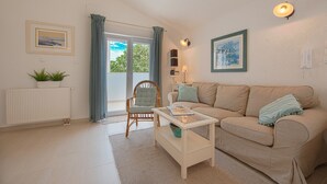A living room with a beige sofa, a white coffee table, a wicker chair, a radiator, and a window with curtains. - Spacious Chic Residence (Zadar)