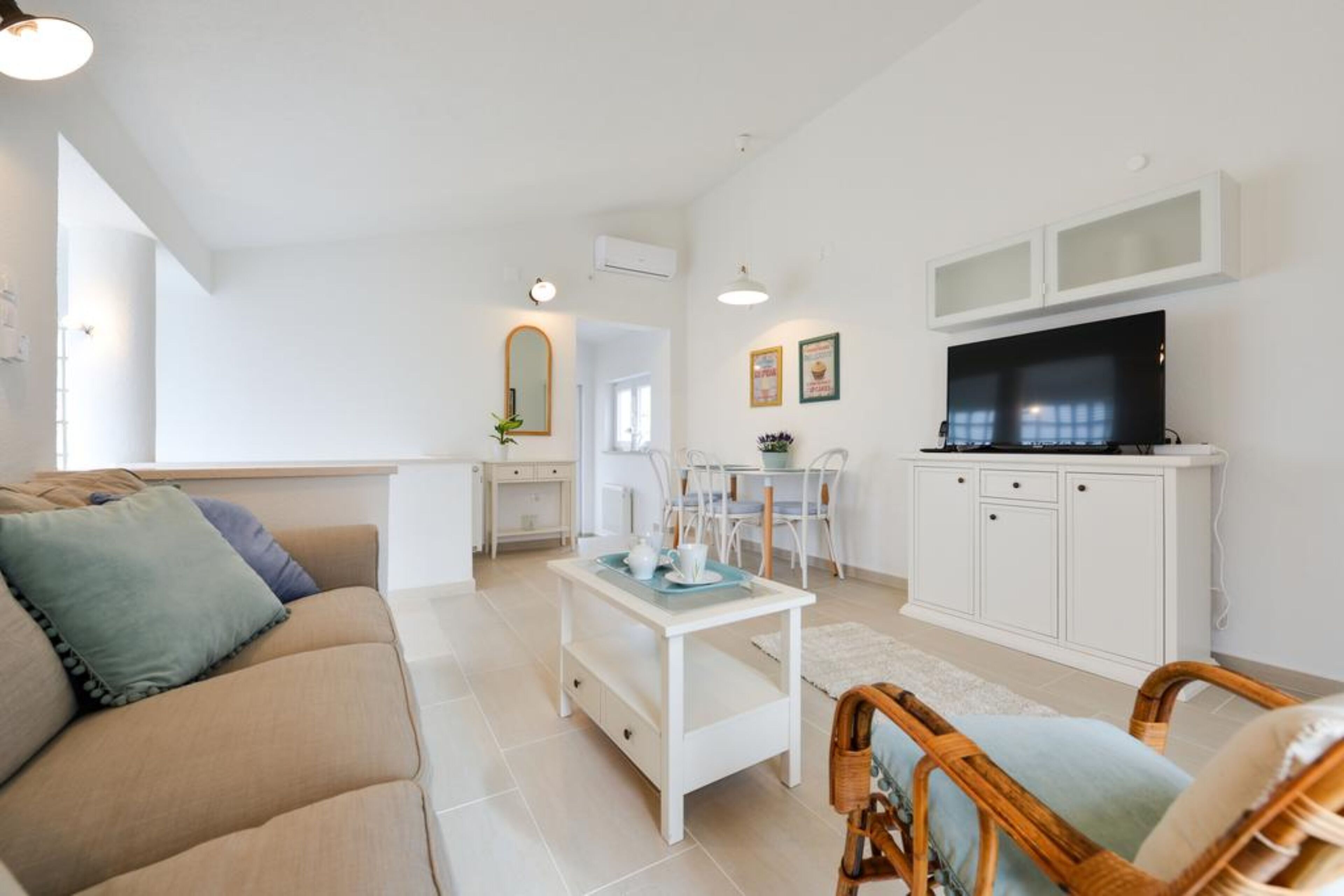 Un salon moderne avec un canapé beige, une table basse blanche et un téléviseur posé sur un meuble blanc.