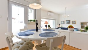 A dining area with a round table, chairs, and blue placemats. There is a bottle of wine and a glass on the table. - Spacious Chic Residence (Zadar)