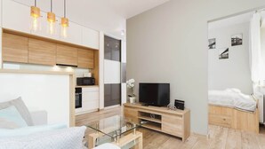 A modern living room with a glass coffee table, a flat-screen TV, and a sofa. There is a wooden cabinet with built-in lighting and a small plant on the side. - Modern Apartment | Parking | Close to Tauron Arena (Kraków)