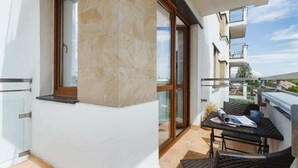 A balcony with a glass door, a small table with a magazine, and wicker furniture. - Modern Apartment | Parking | Close to Tauron Arena (Kraków)