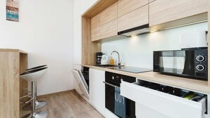 A modern kitchen with wooden cabinets, a black microwave, a coffee maker, and a dishwasher. - Modern Apartment | Parking | Close to Tauron Arena (Kraków)