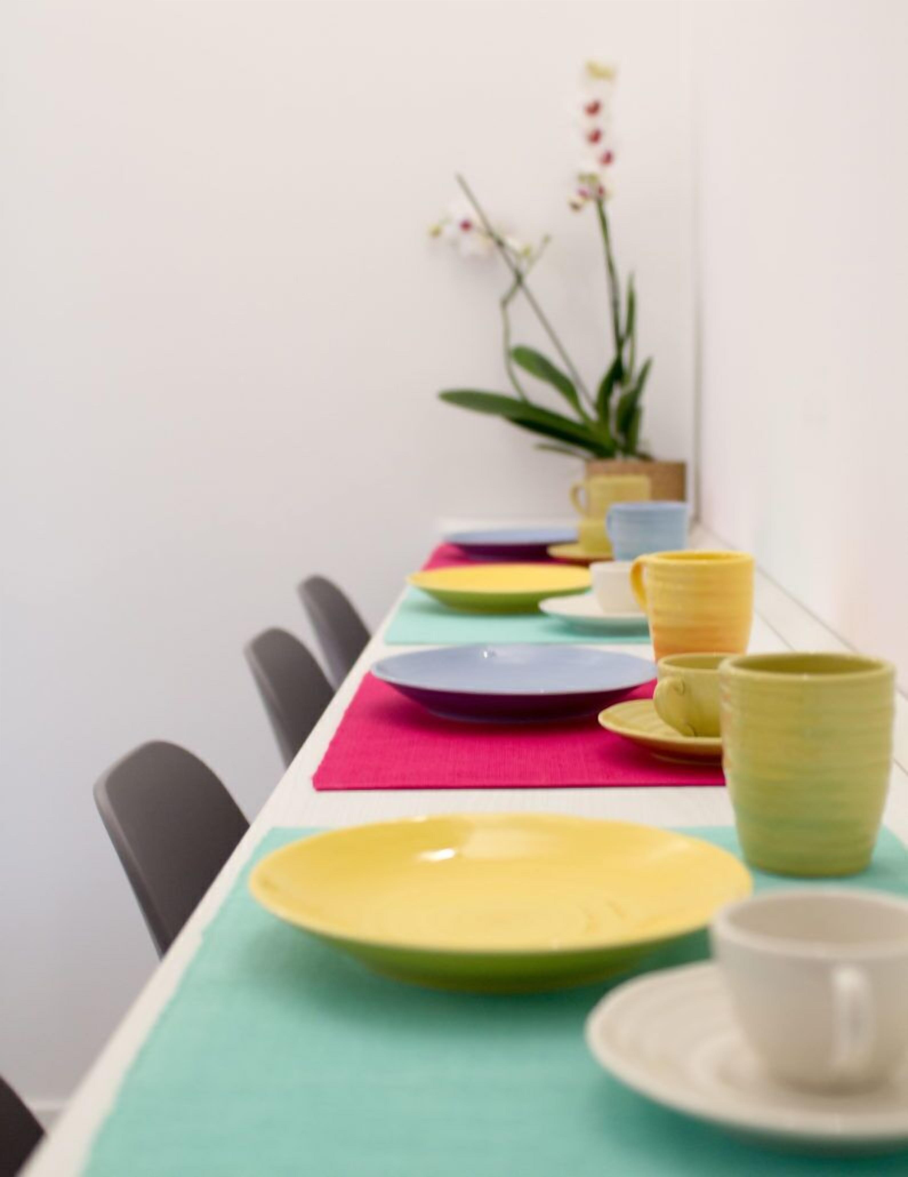 A dining table with colorful plates and cups, chairs, and a potted plant.