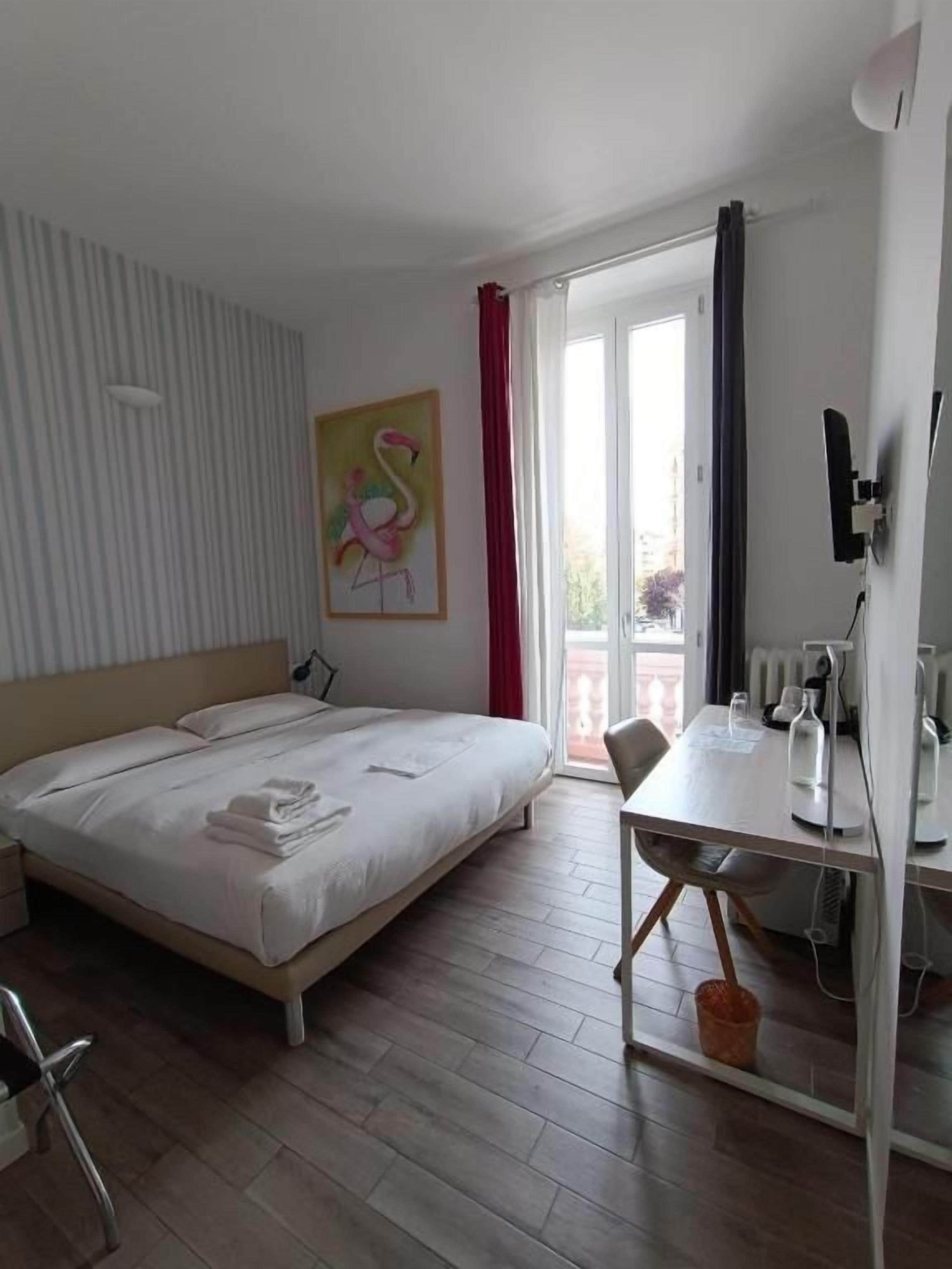 Une chambre d’hôtel avec un lit, un bureau, une chaise, une fenêtre avec des rideaux et un tableau au mur.