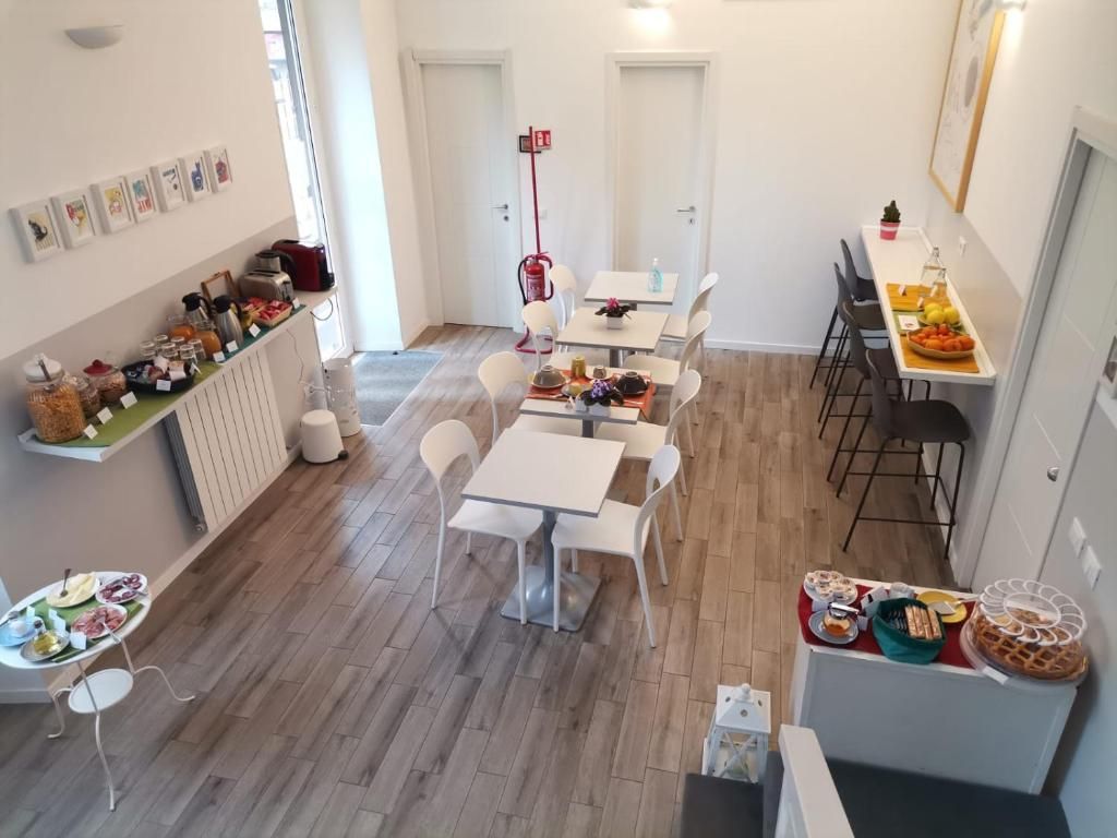 A dining area with multiple tables and chairs, a kitchen counter with food items, and a wall with framed pictures.