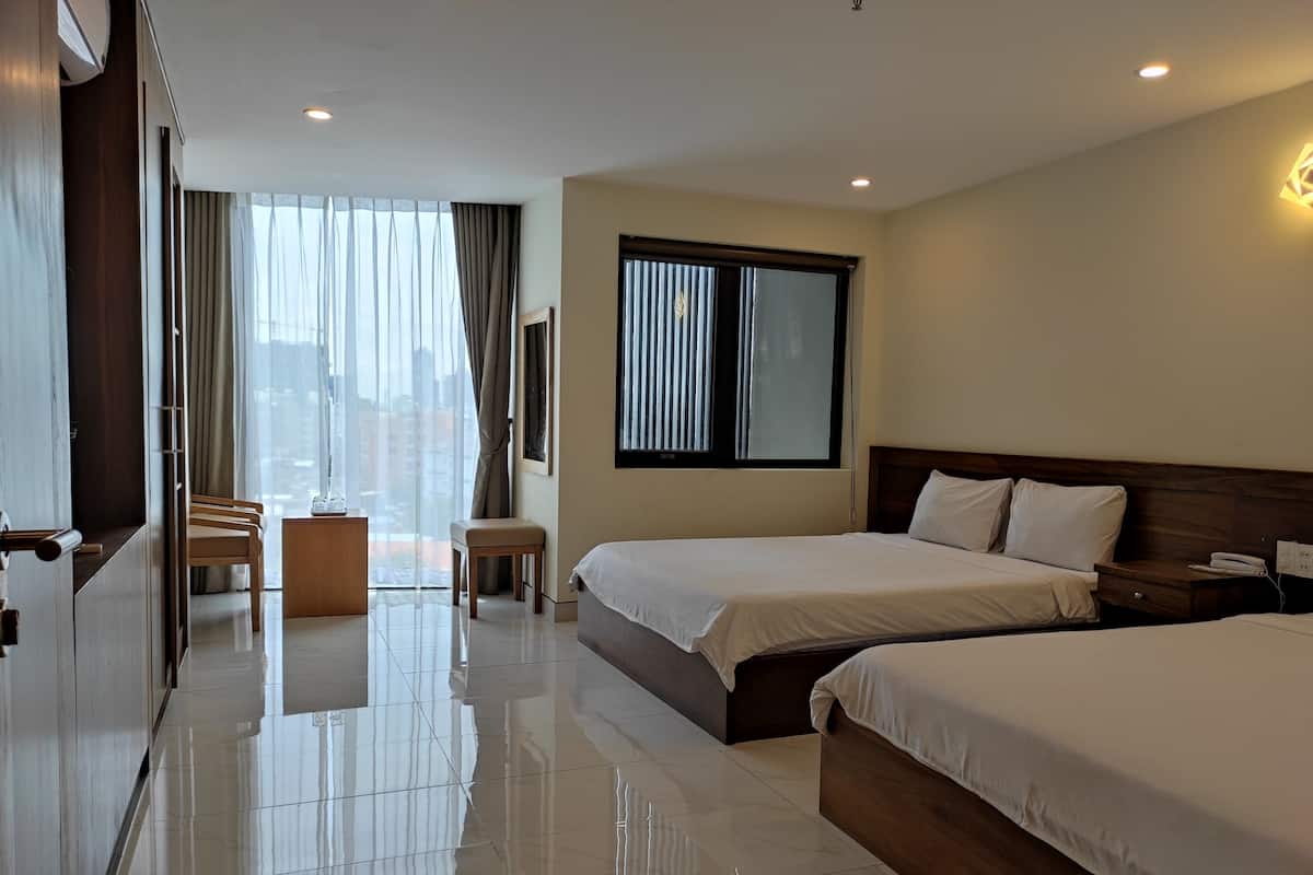 A hotel room with two beds, a desk, a chair, and a large window with curtains.