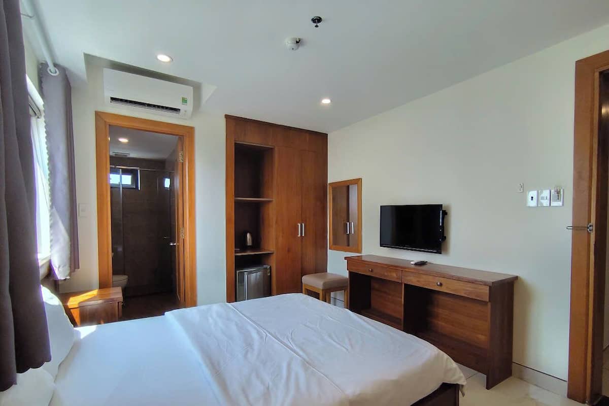 A hotel room with a large bed, a wooden desk, a television, and a wardrobe.