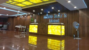 A hotel reception area with a modern design, featuring a wooden reception desk, a glass partition, and a ceiling with illuminated panels. - Hong Hai 2 Hotel (Ho Chi Minh City)