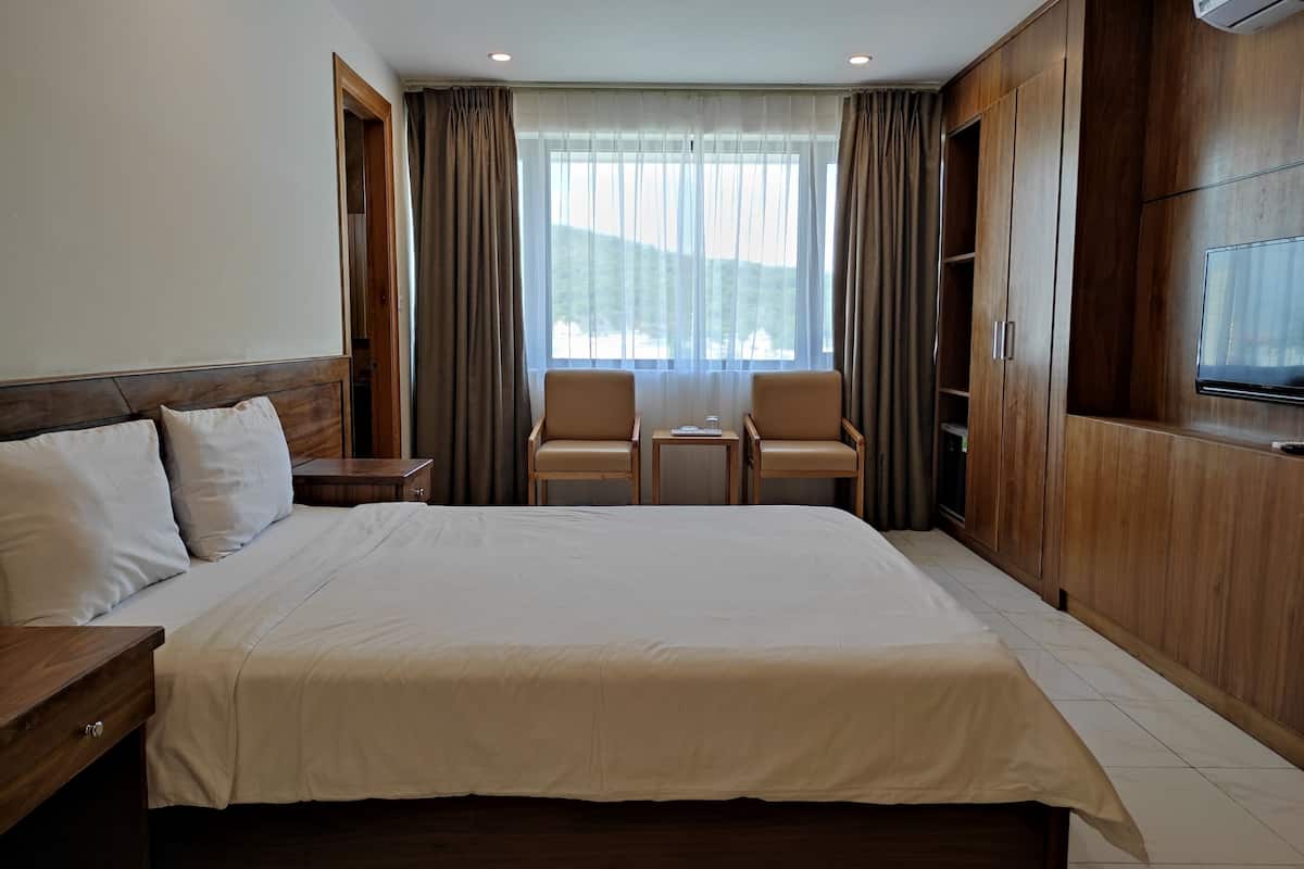 A hotel room with a large bed, two armchairs, a small table, and a TV.