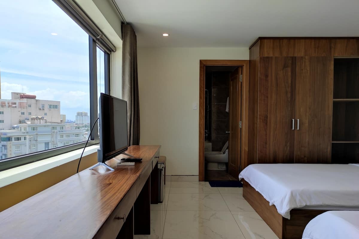 A hotel room with a wooden desk, a bed, and a view of the city.