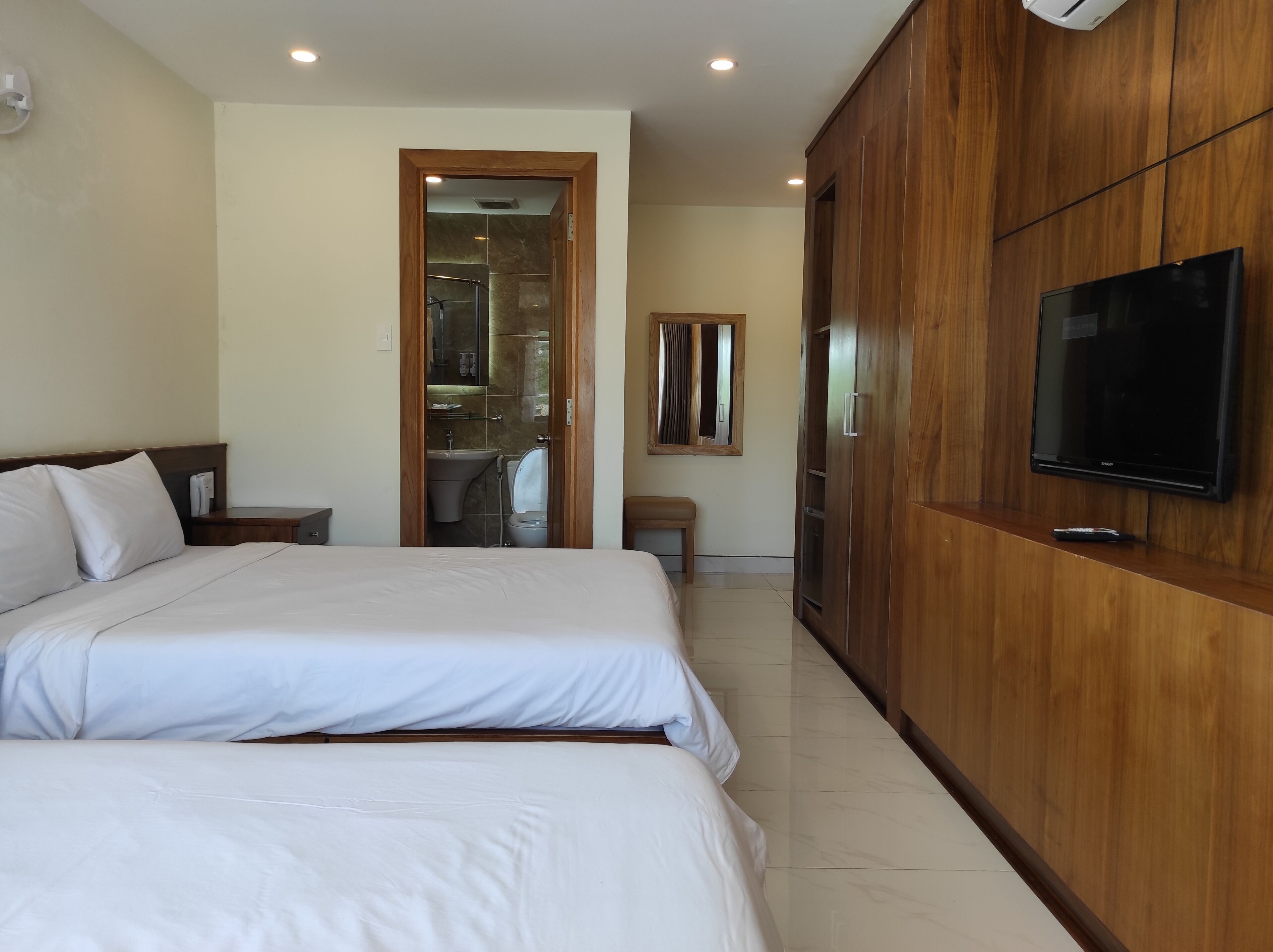 A hotel room with two beds, a wooden wardrobe, a television, and a bathroom visible through an open door.