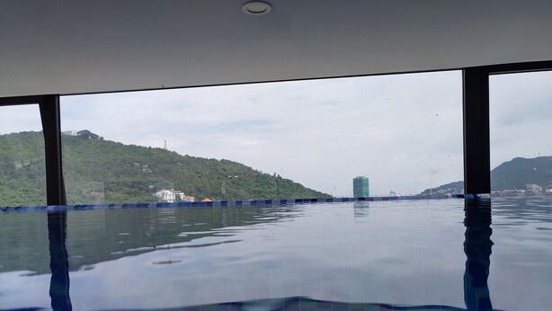 A view from a window with a pool in the foreground, a body of water, and a green hillside with buildings in the background. - Hong Hai 2 Hotel (Ho Chi Minh City)