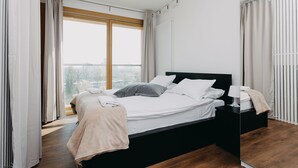 A modern bedroom with a large bed, a nightstand, and a view of the city through a large window. - ShortStayPoland Kolejowa - B10 (Warsaw)