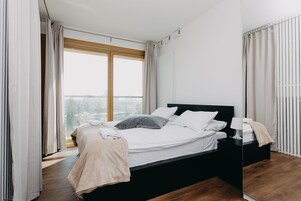 Moderni makuuhuone, jossa on suuri sänky, yöpöytä ja suuri ikkuna, josta avautuu näkymä kaupunkiin.