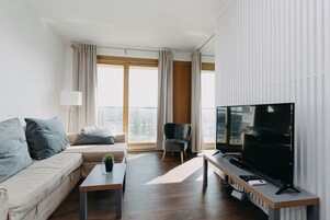 Moderni olohuone, jossa on sohva, sohvapöytä, televisio ja nojatuoli.
