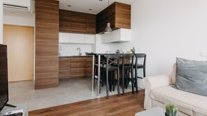 A modern kitchen with wooden cabinets, a dining table with chairs, and a white sofa in the living area. - ShortStayPoland Kolejowa - B10 (Warsaw)
