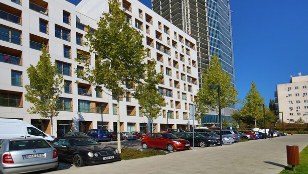 A modern building with multiple floors, a parking area with various cars, and a construction crane in the background. - ShortStayPoland Kolejowa - B10 (Warsaw)