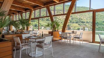 Un área de comedor al aire libre con vigas de madera, ventanas grandes y plantas en macetas.