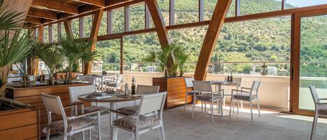 An outdoor dining area with wooden beams, large windows, and potted plants.