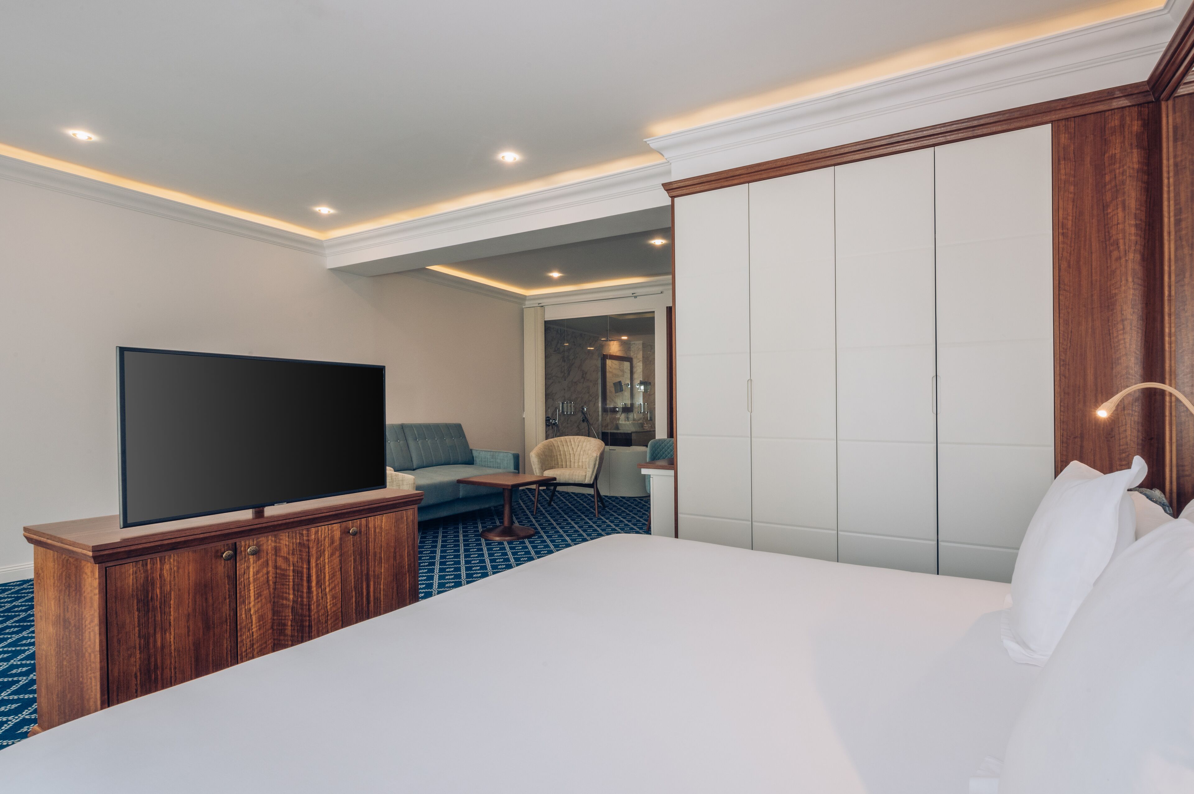 A hotel room with a large bed, a flat-screen TV on a wooden cabinet, a sofa, and a small table.