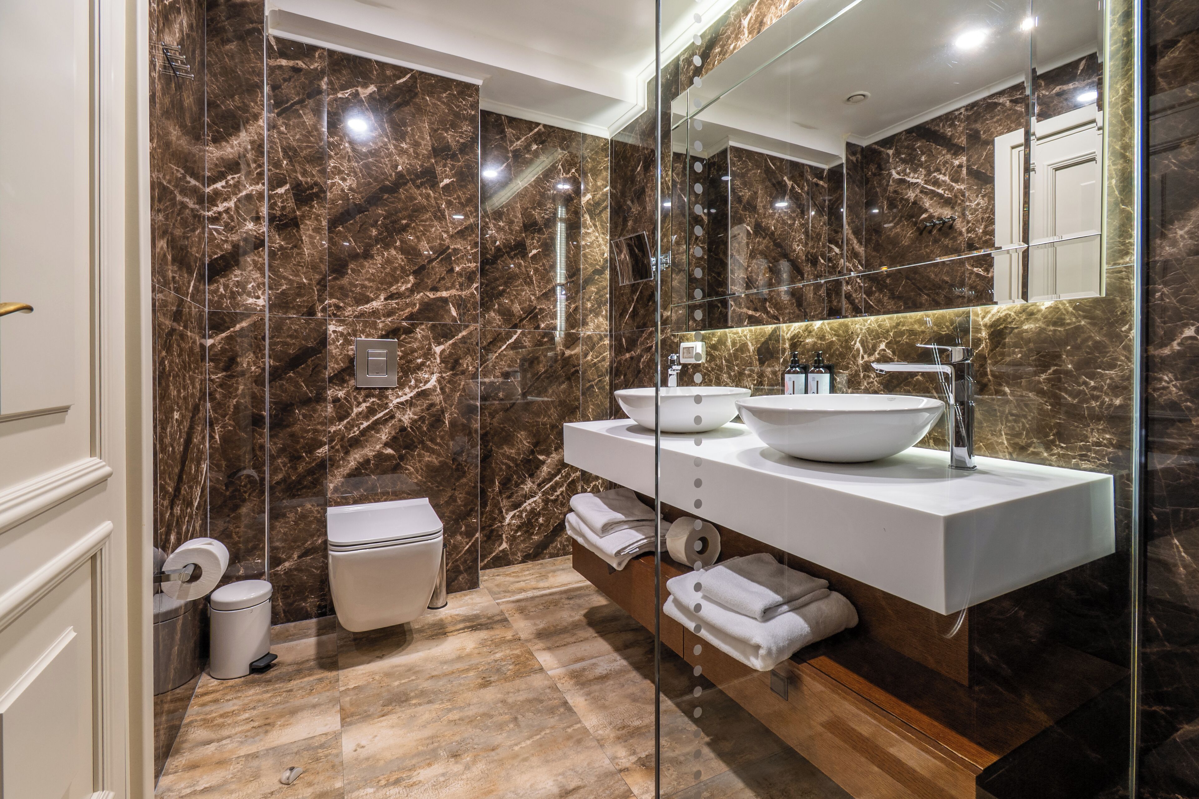 A modern bathroom with a large mirror, a vessel sink, and marble walls.