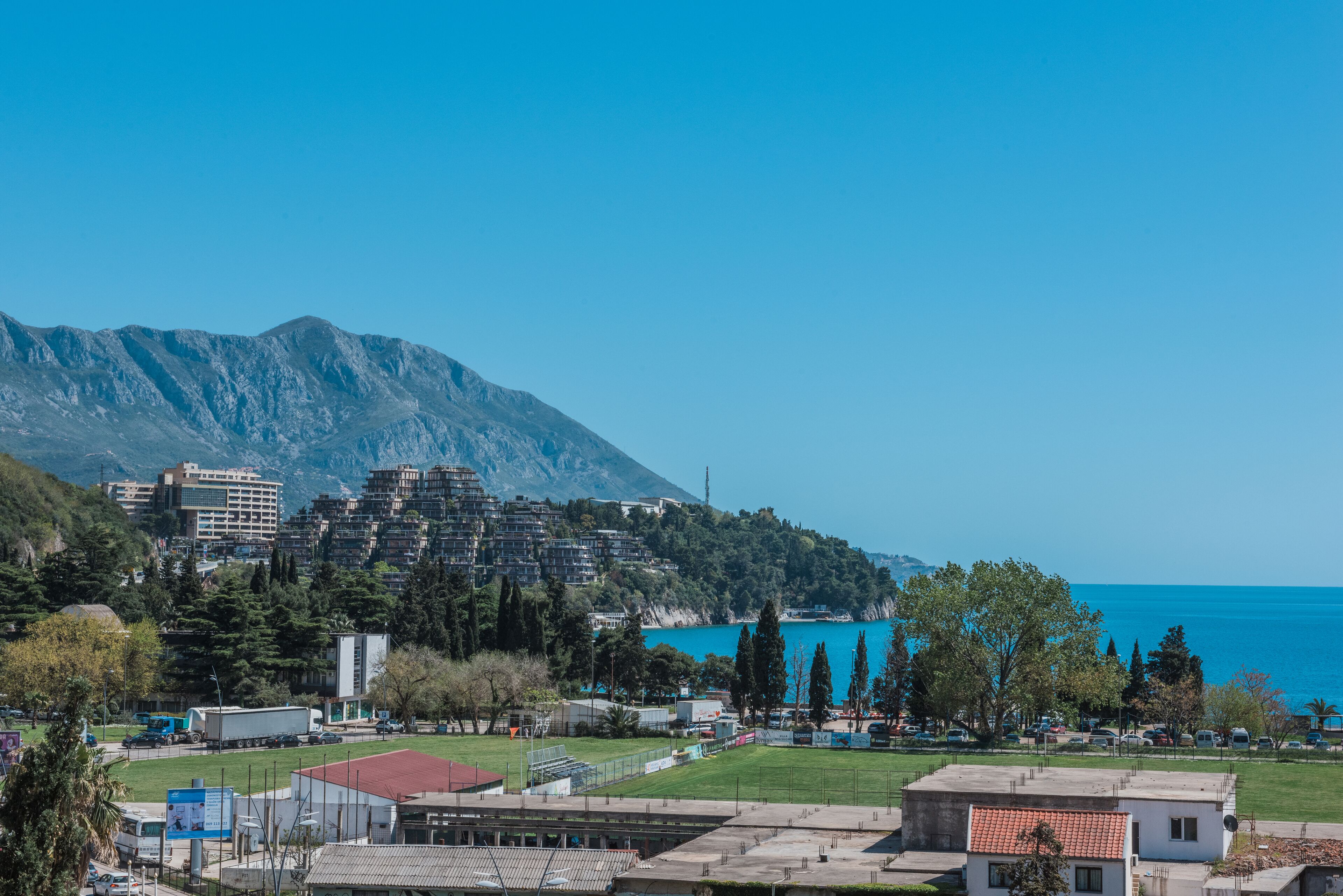 Eine Küstenstadt mit Bergblick, mit Wohnhäusern, einem Sportplatz und freiem Blick auf das Meer.