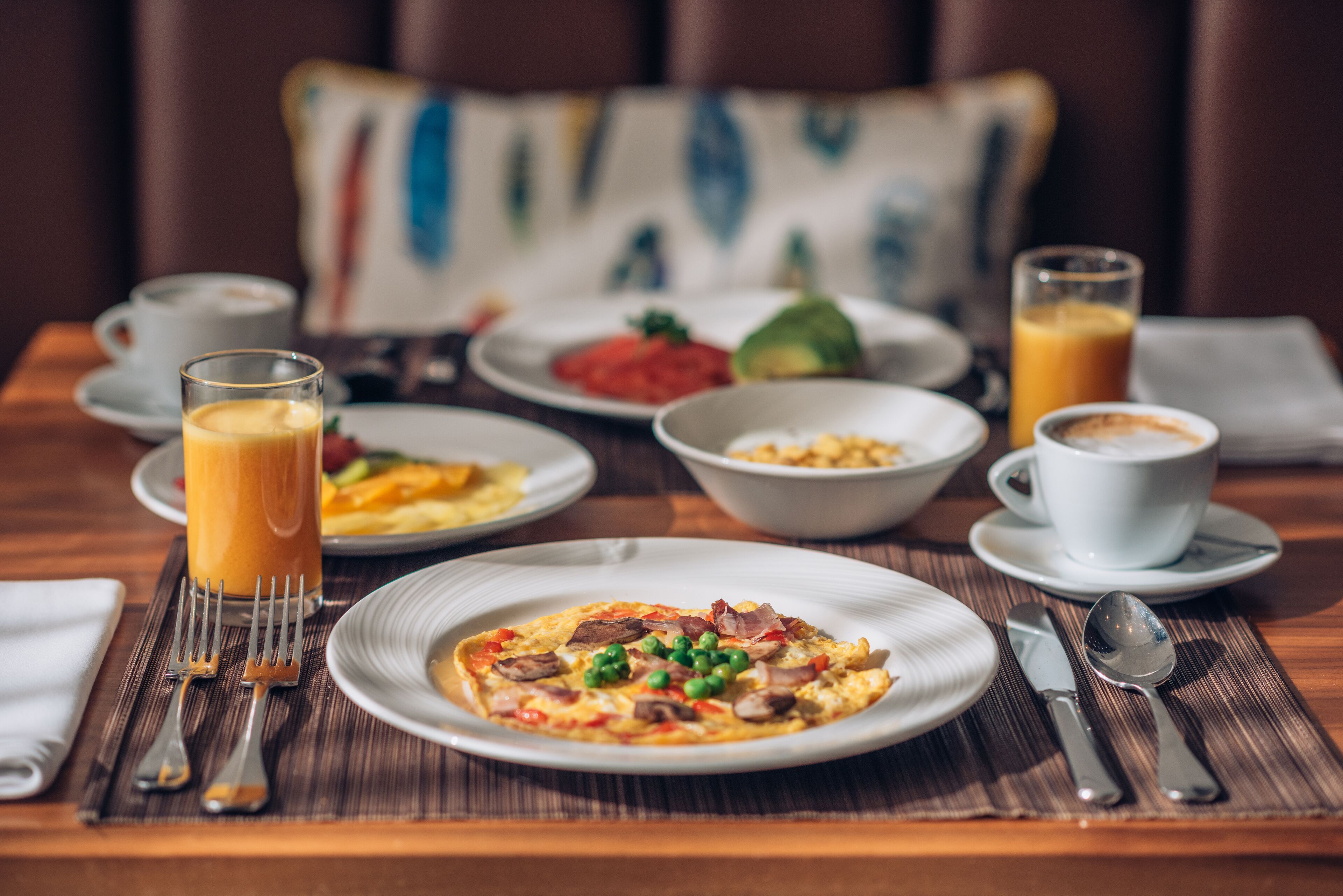 Una escena de desayuno con platos de comida, un vaso de jugo de naranja y una taza de café sobre una mesa de madera.