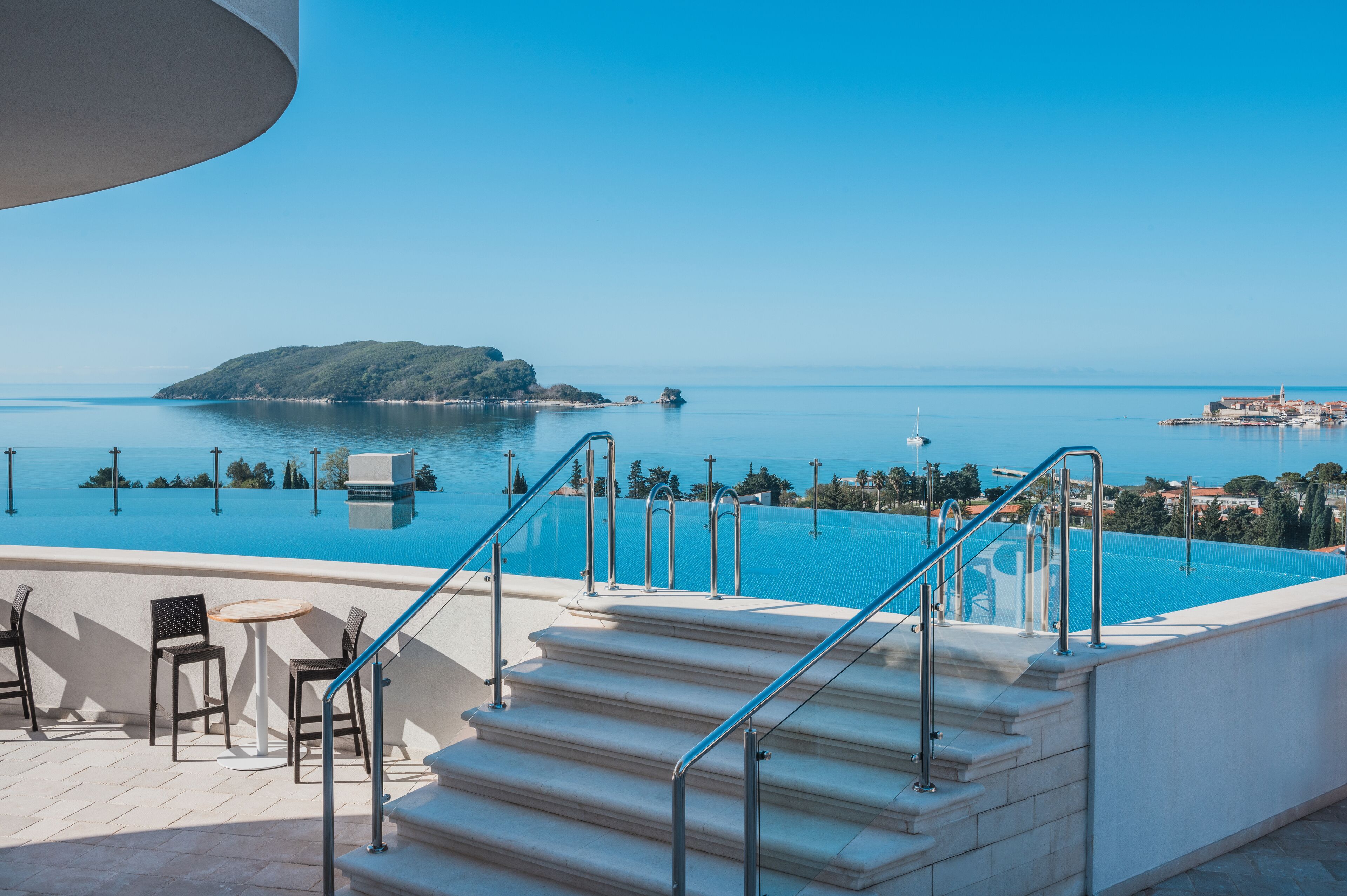 Un espace piscine avec des marches menant à une terrasse d’où l’on a vue sur une étendue d’eau et une île lointaine.