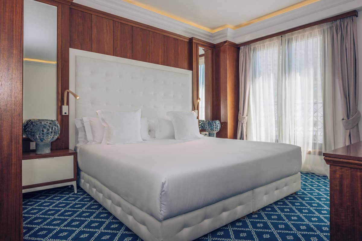Ein großes Bett mit einem gepolsterten Kopfteil, ein Nachttisch mit einer Vase und ein großer Spiegel.